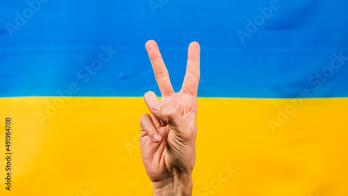 Hand in victory symbol with Ukrainian flag for background