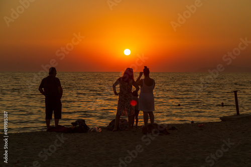 tourists sunbatting under straw umbrellas. REflection of amazing sunset © Birol