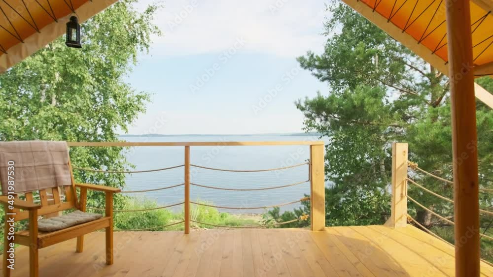 Dollying in view from wooden terrace on second floor of summer house of beautiful lake, wild beach and trees on sunny day Dollying in view from wooden terrace on second floor of summer house of beautiful lake, wild beach and trees on sunny day