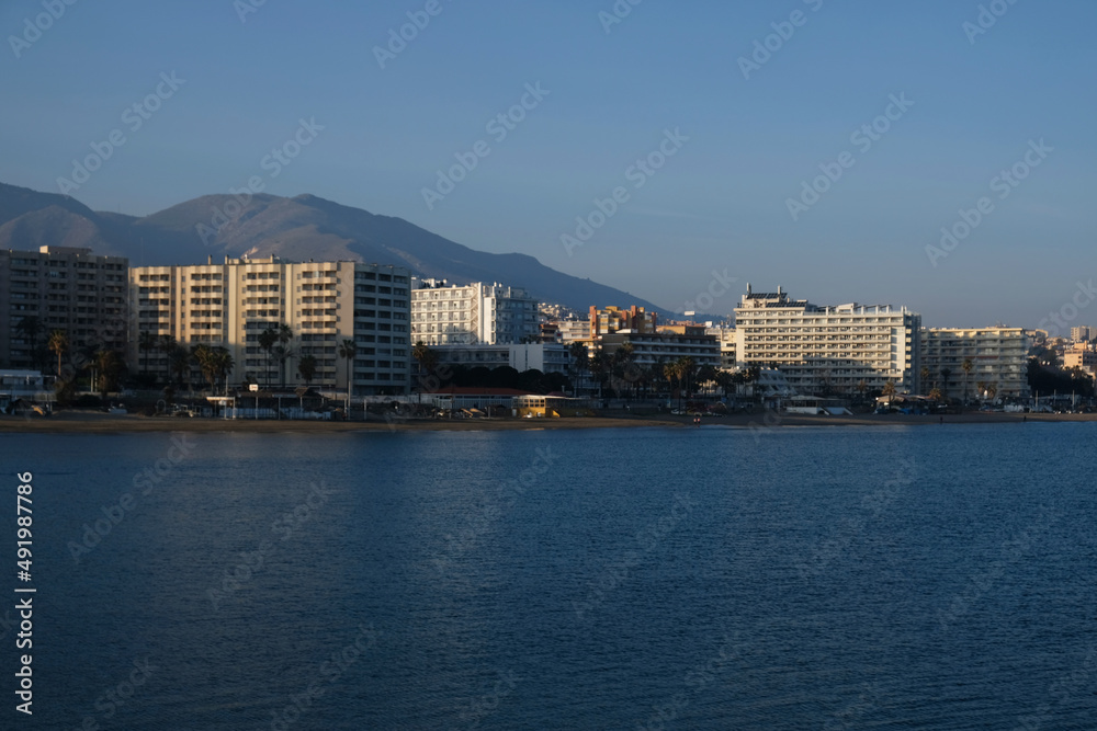 View of high-rise resort hotels or residential buildings on Mediterranean coast in Malaga, Andalusia, Spain. View of sandy beach, palm trees, blue sea, blue sky and mountains. Real estate concept.