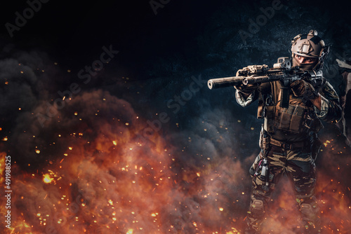 Army soldier with rifle aiming against dark flaming background © Fxquadro