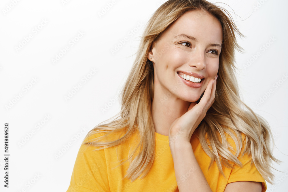 Beauty and haircare. Attractive young woman with natural blond hair waving flying in air, looking stunning at camera, posing against white background in yellow t-shirt Beauty and haircare. Attractive young woman with natural blond hair waving flying in air, looking stunning at camera, posing against white background in yellow t-shirt