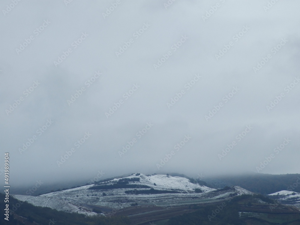 mountain landscape in winter cloudy day covered with snow and foggy land seen from above