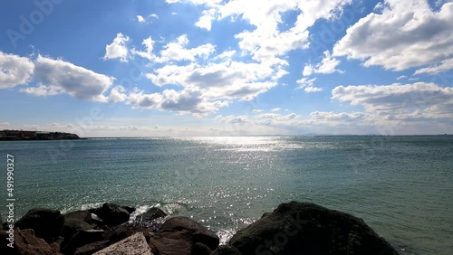 Time-lapse of a seascape on a clear sunny day, clouds descend low over the water in dynamic motion, sunlight reflects on the water, motionless rocks in the foreground