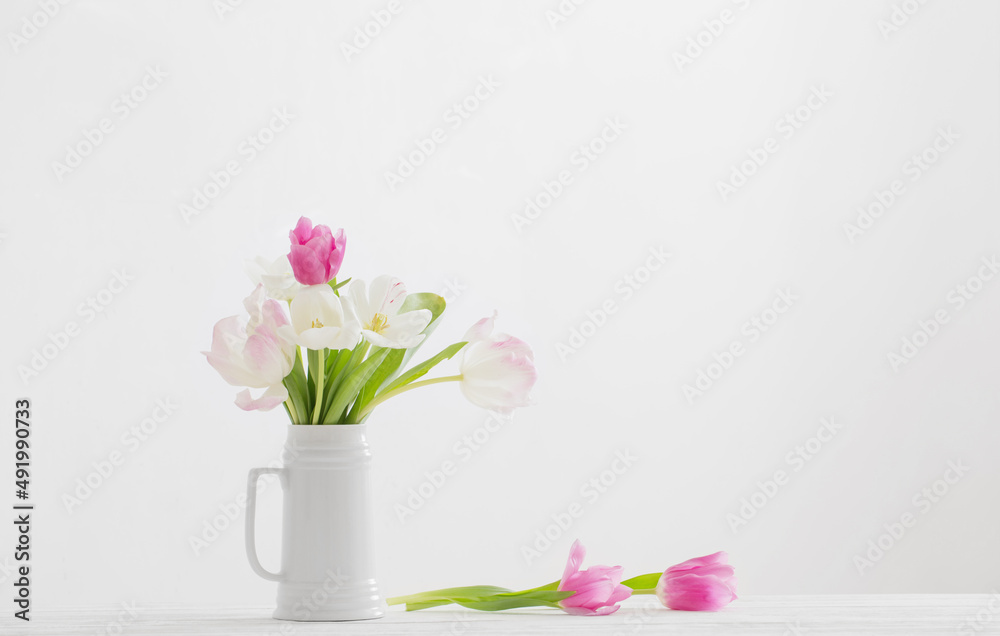 white and pink tulips in jug on white background