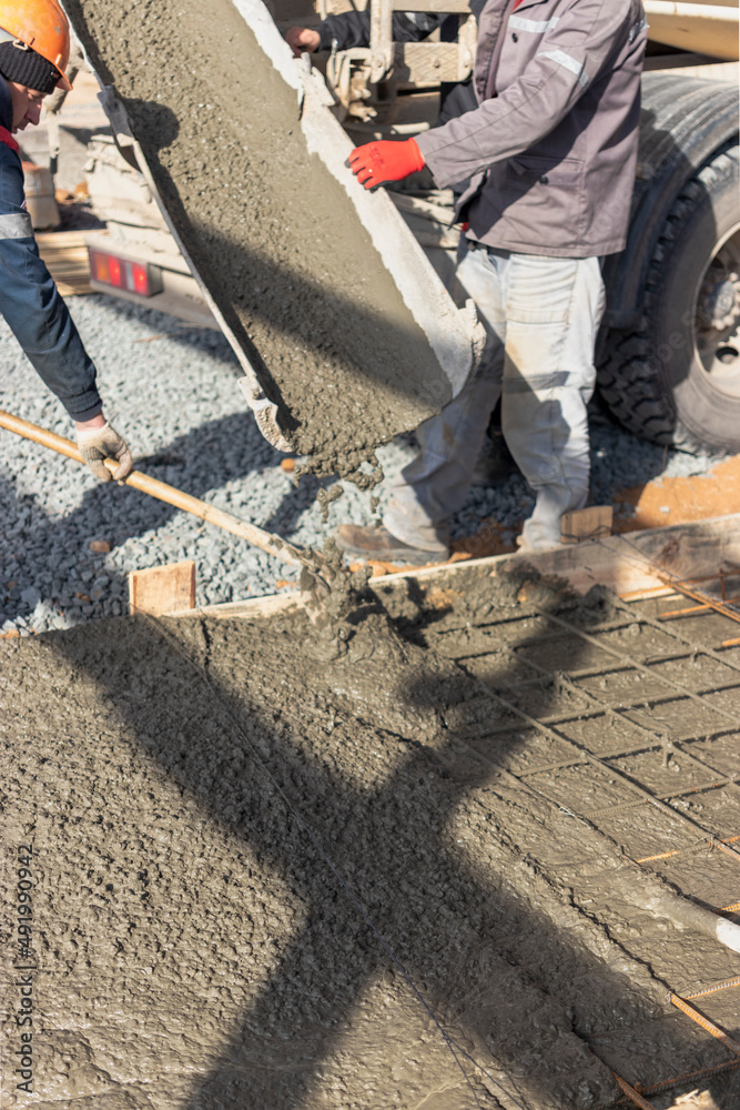 Pouring cement or concrete with a concrete mixer truck, construction site with a reinforced grillage foundation. Workers settle and level the concrete in the foundation. Pouring cement or concrete with a concrete mixer truck, construction site with a reinforced grillage foundation. Workers settle and level the concrete in the foundation.