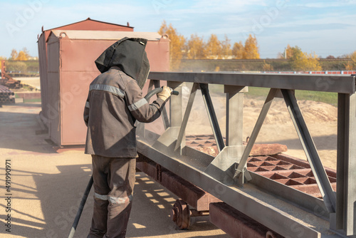 Foto A worker in special clothing is sandblasting a metal building structure at an industrial site