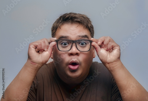 Asian man showing surprise, shock, excitement and hand-holding glasses on a gray background.