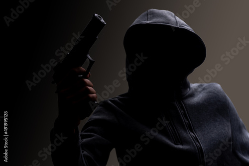 Photo of a creepy horror criminal in black hoodie holding revolver gun.