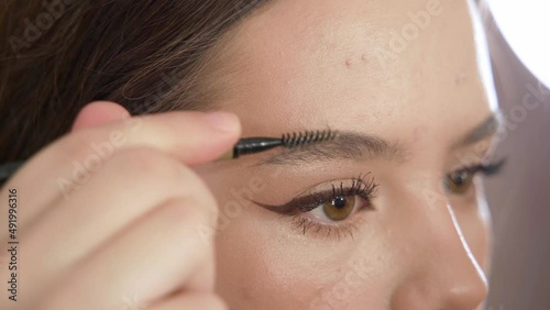 A young beautiful girl does makeup in the studio paints eyelashes, eyebrows, lips looks in the mirror close-up. Makeup of a girl's face close-up in the studio in front of a mirror.
