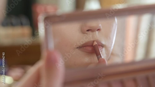 A young beautiful girl does makeup in the studio paints eyelashes, eyebrows, lips looks in the mirror close-up. Makeup of a girl's face close-up in the studio in front of a mirror.