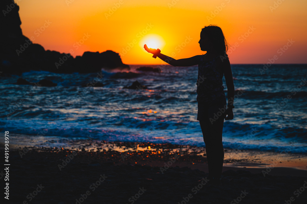 Silhouette of a child holding sun in hand on a beach.