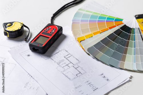 Tools for the work of an interior designer on the table. Color palette, laser tape measure and house plan drawings. Close-up.
