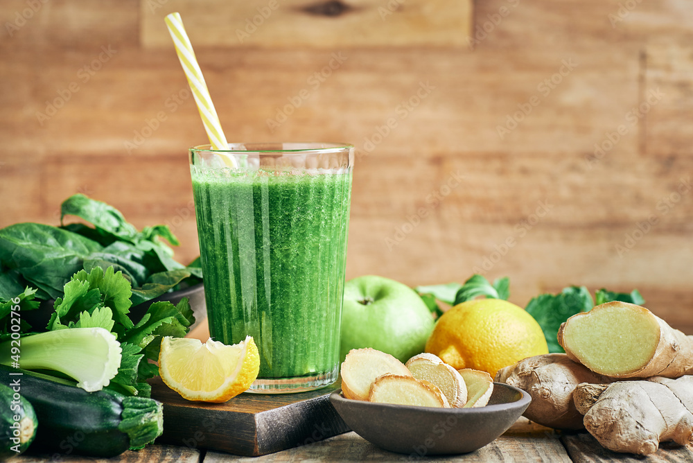 Fototapeta premium Fresh green vegan detox smoothie with ginger. Fresh healthy ginger green vegetables smoothie served in glass with lemon for diet and detox.
