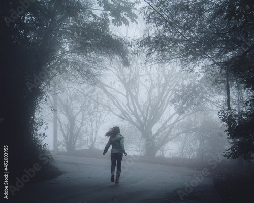 silhueta de mulher correndo entre árvores cobertas pela neblina