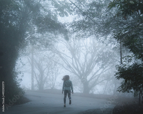 silhueta de mulher correndo entre árvores cobertas pela neblina