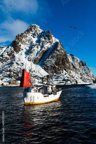 Łódź rybacka wypływa na połów dorsza na morzu norweskim u wybrzeży Lofotów w północnej Norwegii, w tle duża, ośnieżona góra