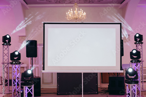 Party setting. A view to the projection screen equipment at the decorated background of a banquet hall. Facilities for video and audio projection at a festive event. Show arrangement at a banquet