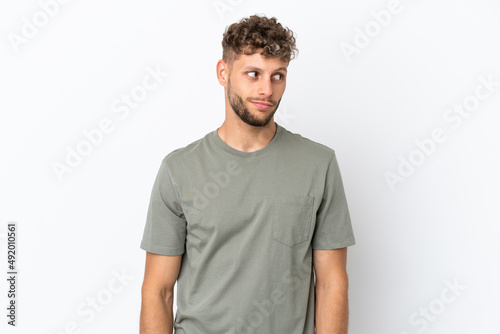 Young caucasian handsome man isolated on white background making doubts gesture looking side