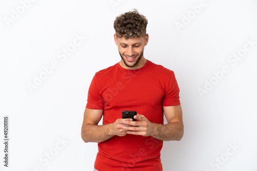 Young caucasian handsome man isolated on white background sending a message with the mobile © luismolinero