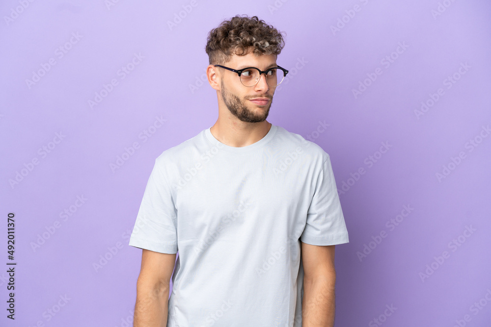 Fototapeta premium Delivery caucasian man isolated on purple background making doubts gesture looking side