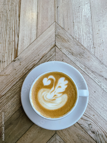 A mug of flat white or latte art coffee on a wooden table. Coffee art. Directly above. Swan shape