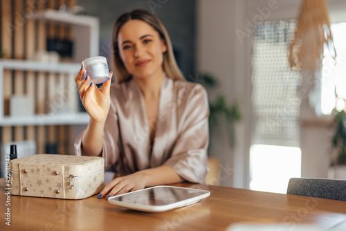 Portrait of a smiling girl, holding cream for the face, promotin