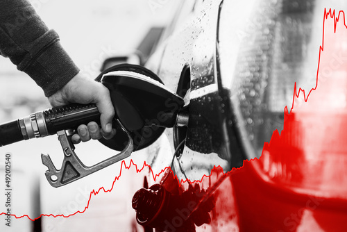 Hand with fuel nozzle and rising chart showing gasoline price increase during energy crisis photo
