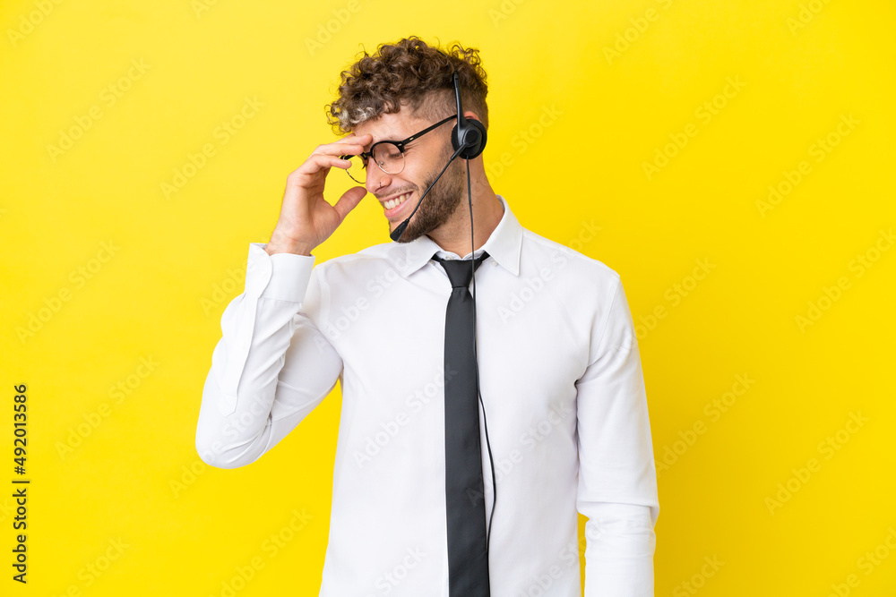Telemarketer blonde man working with a headset isolated on yellow background laughing