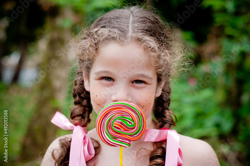 Portrait of beautiful girl with pigtails showing a lollipop at the camera, focus on the girl