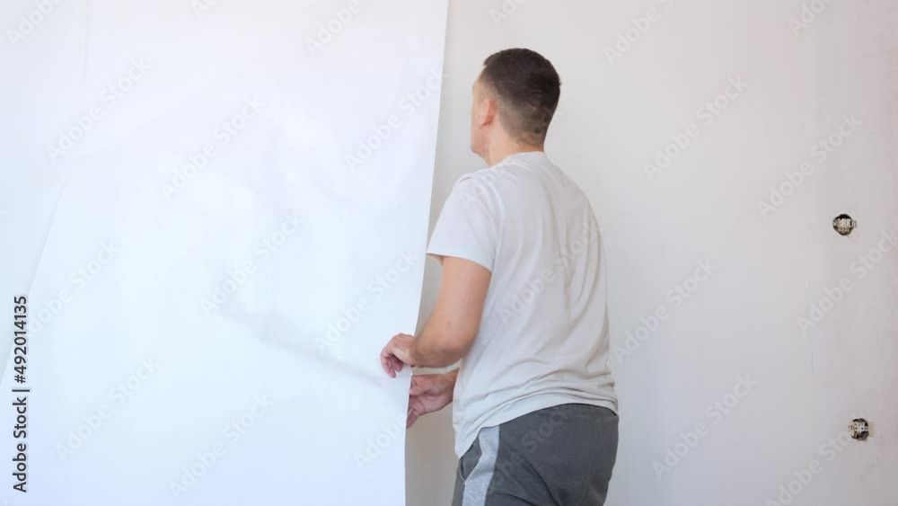Process of removing old white wallpaper from the wall in the room during repairs at home. Caucasian man remove old wallpapers from wall. Process of removing old white wallpaper from the wall in the room during repairs at home. Caucasian man remove old wallpapers from wall.