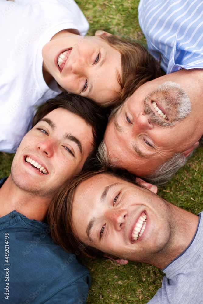 Laughing together through the ages. Father and sons lying down on the grass with their heads beside one another. Laughing together through the ages. Father and sons lying down on the grass with their heads beside one another.
