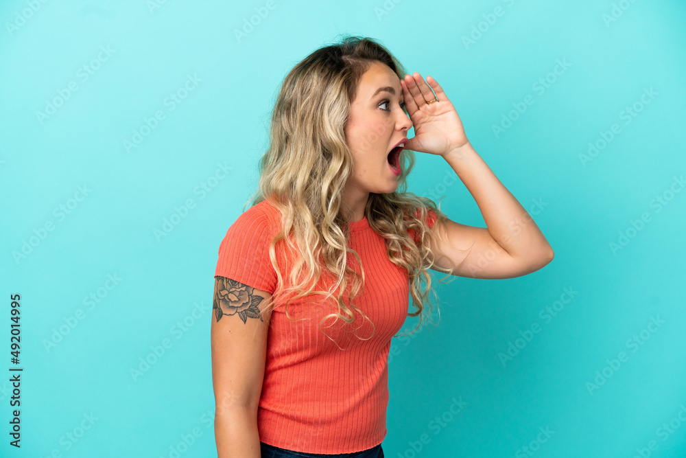 Young Brazilian woman isolated on blue background with surprise expression while looking side