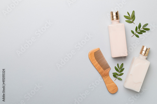 Shampoo and conditioner with herbal extract and comb on color background, top view