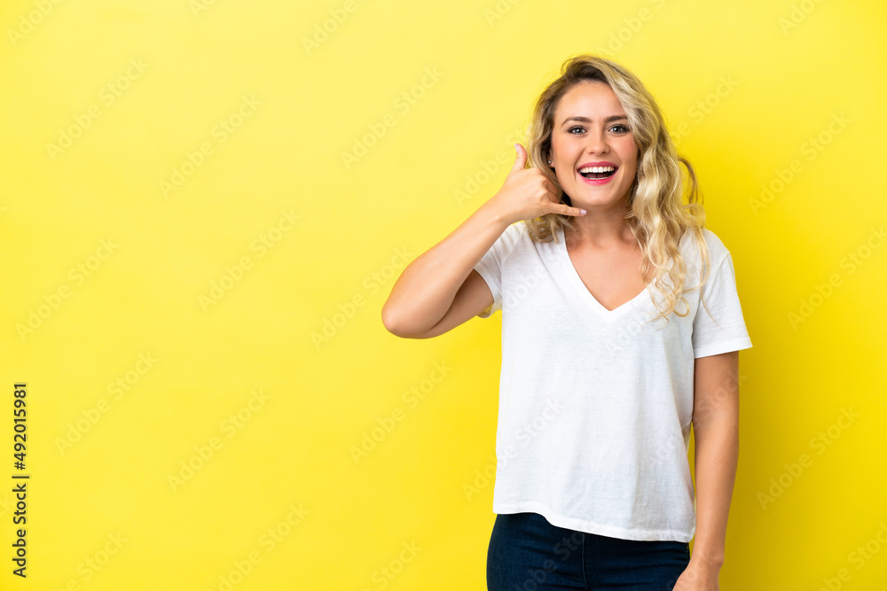 Young Brazilian woman isolated on yellow background making phone gesture. Call me back sign Young Brazilian woman isolated on yellow background making phone gesture. Call me back sign