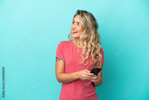 Young Brazilian woman isolated on blue background using mobile phone and looking up © luismolinero