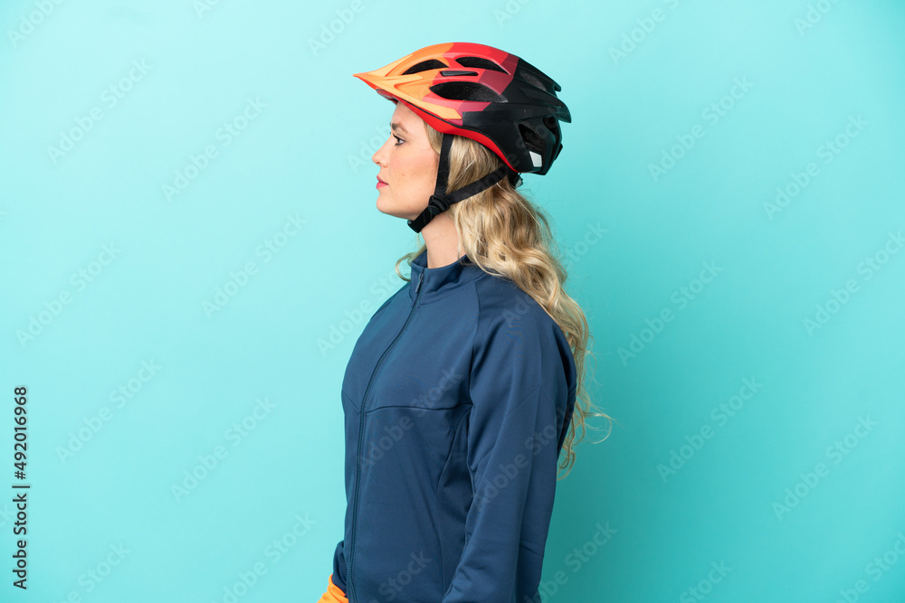 Young cyclist woman isolated on blue background looking to the side Young cyclist woman isolated on blue background looking to the side
