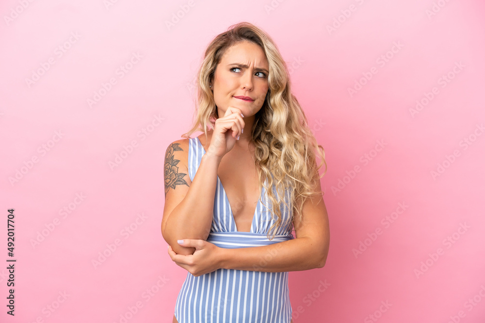 Young Brazilian woman in swimsuit in summer holidays isolated on pink background having doubts and thinking Young Brazilian woman in swimsuit in summer holidays isolated on pink background having doubts and thinking