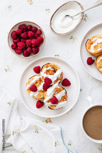 Cottage cheese pancakes in white plate. Syrniki with raspberries and sour cream. Homemade breakfast or lunch.