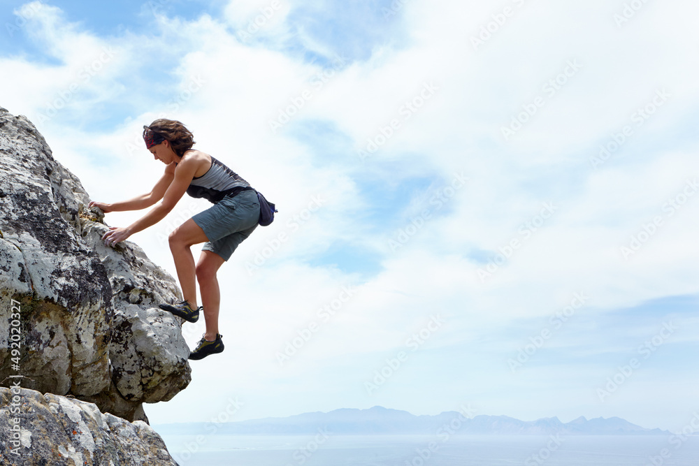 Theres no mountain too high. A woman scaling a rockface on a sunny day. Theres no mountain too high. A woman scaling a rockface on a sunny day.