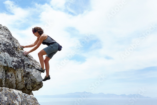 Theres no mountain too high. A woman scaling a rockface on a sunny day.