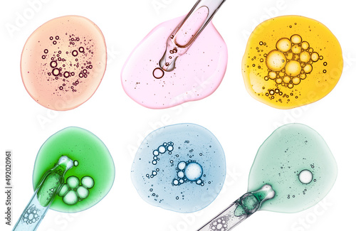 Liquid assortment yellow, orange, blue retinol, rose or vitamin c gel or serum with a dropper on a screen of microscope white isolated background photo