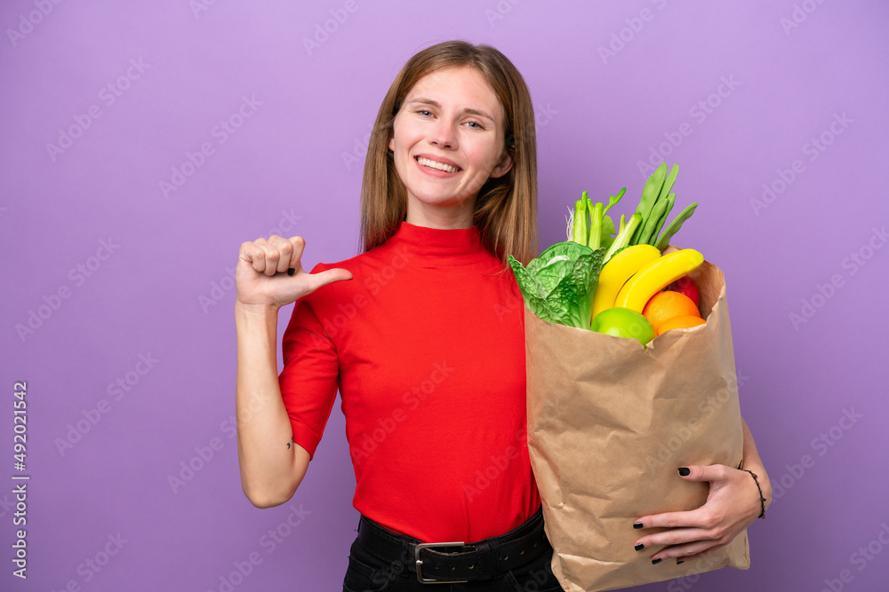 Young English woman holding a grocery shopping bag isolated on purple background proud and self-satisfied Young English woman holding a grocery shopping bag isolated on purple background proud and self-satisfied