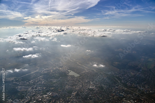 Aerial view from airplane window at high altitude of distant city covered with layer of thin misty smog and distant clouds