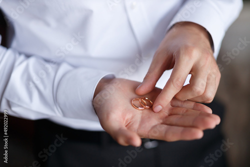 the groom in a white classic shirt with sleeves holds wedding gold rings on his palm, close-up without a face