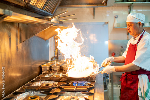Fotografie Indian chef cooking in industrial kitchen with the burning pan