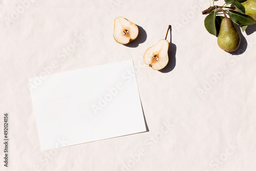 Mockup of white sheet of paper with hard shadows from the sun on a summer day, pear fruit. Stationery. Top view
