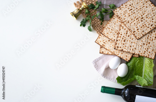 Layout of  Traditional Matzah prepared for Passover with egg, bottle of wine, glass, green salad and parsley on white background. top view. Spring Holiday of Jewish people. Fasting time