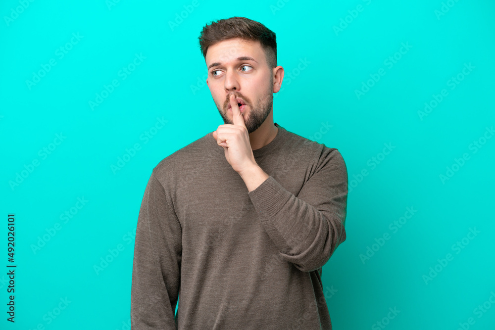Young caucasian man isolated on blue background showing a sign of silence gesture putting finger in mouth Young caucasian man isolated on blue background showing a sign of silence gesture putting finger in mouth