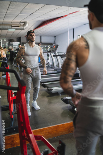 Chico tatuado musculado mirándose y posando delante de un espejo en el gimnasio